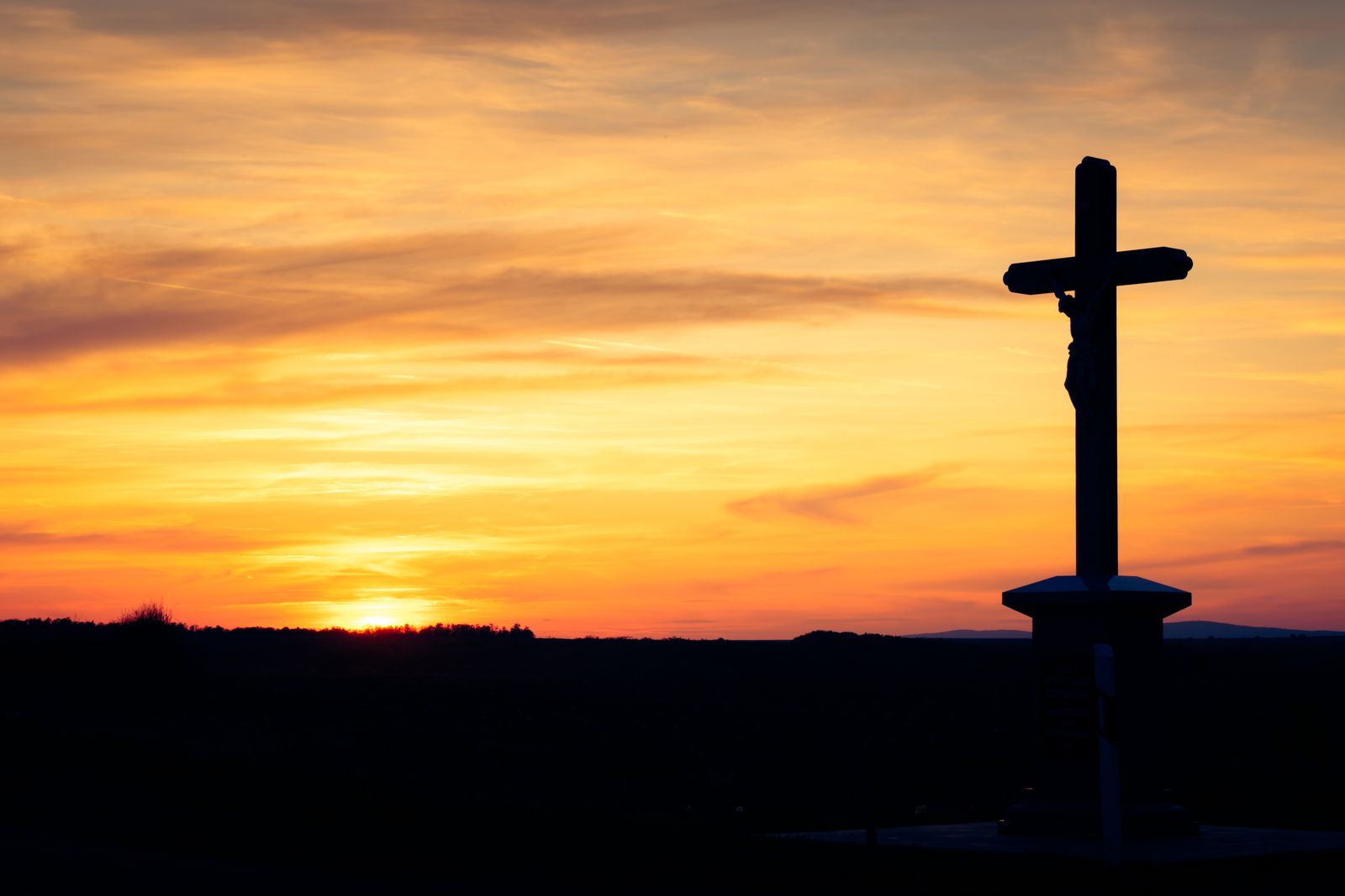Silhueta de uma cruz simples diante do céu ao pôr do sol.